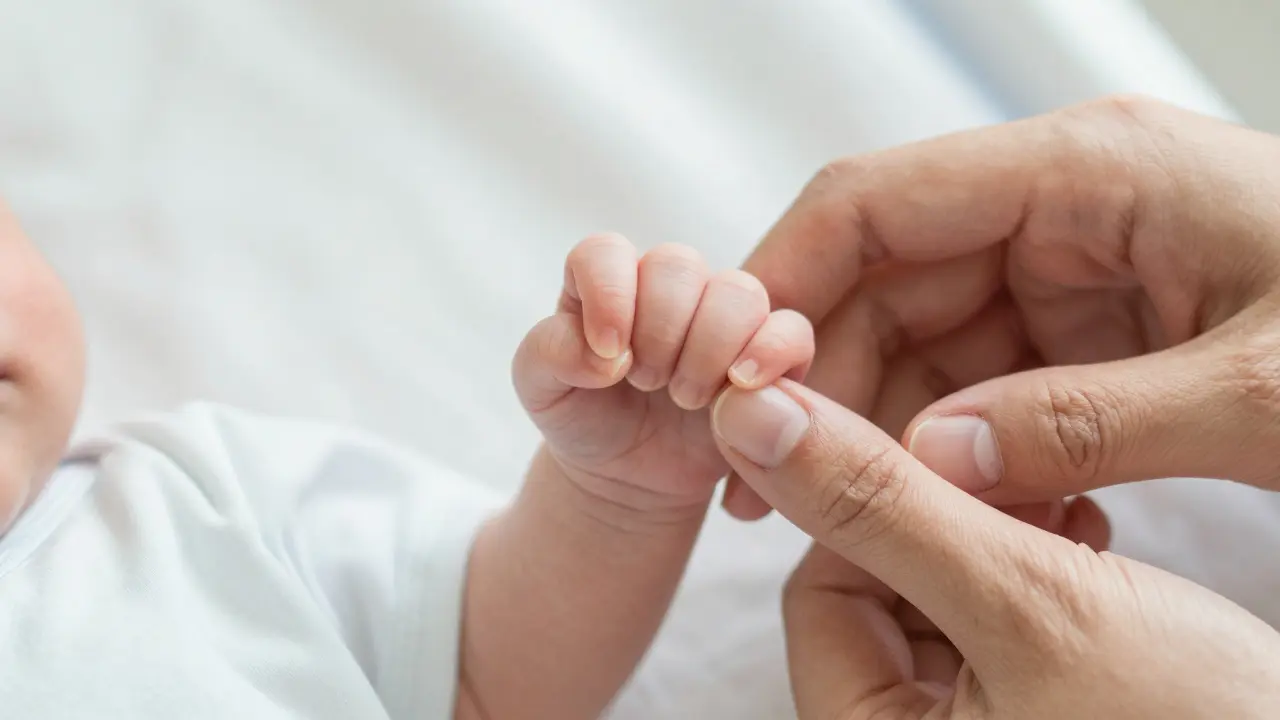 Detail novorozeněte držícího prst matky jako symbol úlevy a radosti.