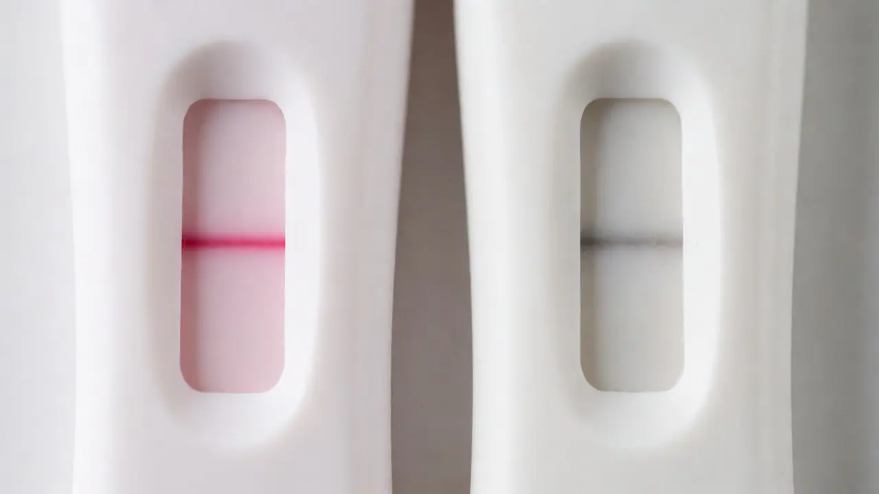 Porovnání dvou těhotenských testů: jasná růžová linka versus bledá šedá čára.